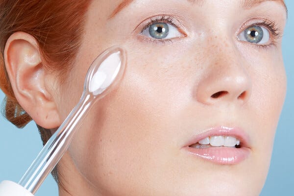 Woman with blue eyes and red hair, holding a High-Frequency A-Home Device next to her face. The woman displays How To Use The High Frequency Device As An Acne Treatment.